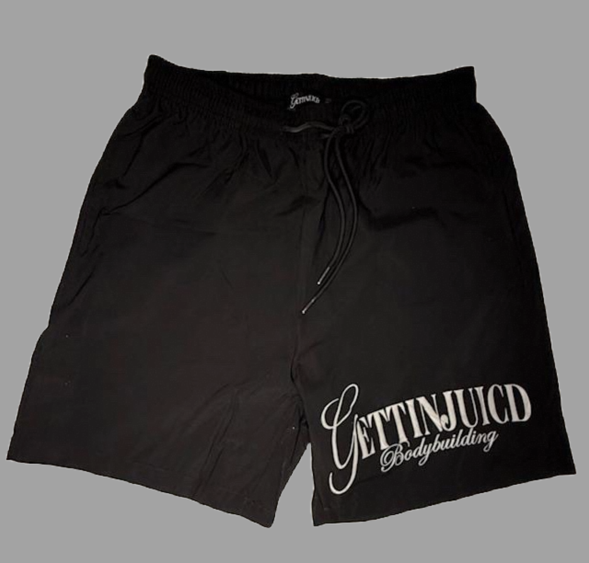 Flat lay of black GettinJuicd men’s gym shorts with drawstring waistband and bodybuilding logo.